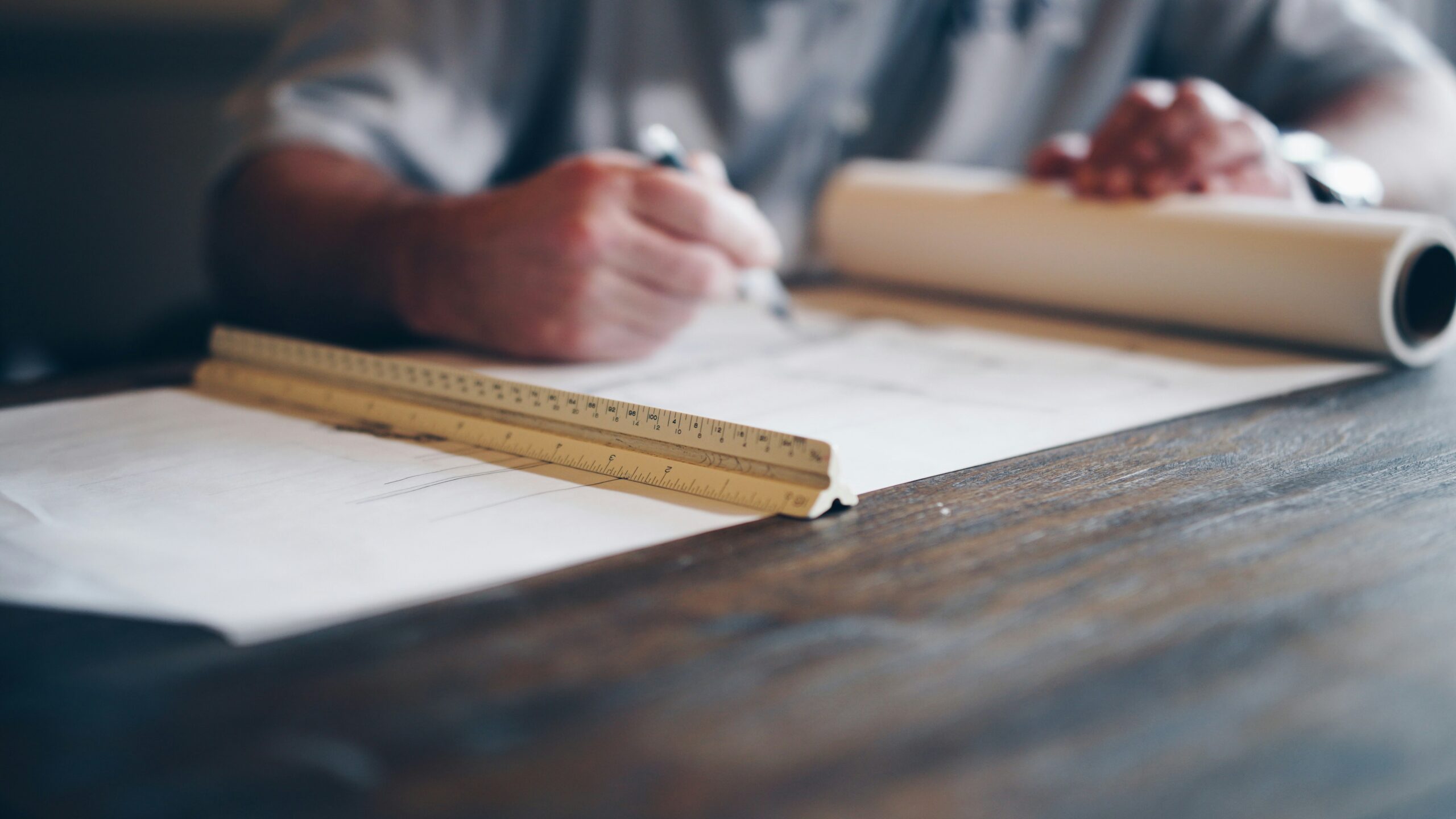 A close up of a person's hands drafting home plans and a drafting ruler.